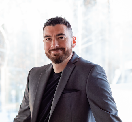 Nic Williams, Fairbanks Alaska real estate broker, smiling in a professional grey suit with natural light background — Your Trusted Real Estate Agent